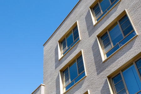Gray brick building corner with large windows under clear blue sky. Architectural detail for...