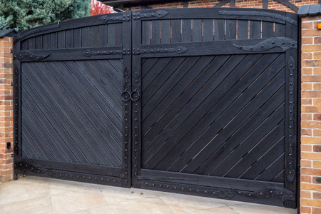 Large black metal driveway gate with diagonal pattern and brick pillars, private property entrance....