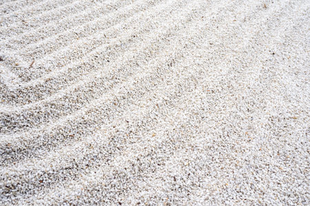 White gravel texture with subtle raked patterns and natural debris. For minimalist backgrounds, construction material visuals, and design projects needing clean, neutral surface detail. Real photo.の写真素材