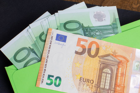 Spread euro banknotes arranged on desk with black wallet, illustrating economic themes such as...