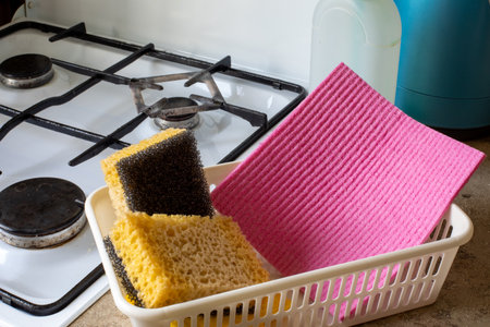 Kitchen sponges and pink scrubber in plastic basket near gas stove. Cleaning supplies, kitchen...