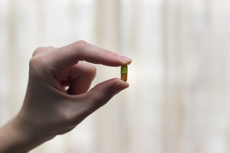 Green and orange capsule with medicine in the woman's hand on a light backgroundの写真素材
