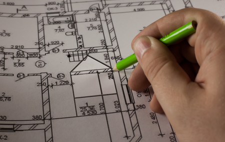 Hand with pencil drawing abstract house on plan of the home