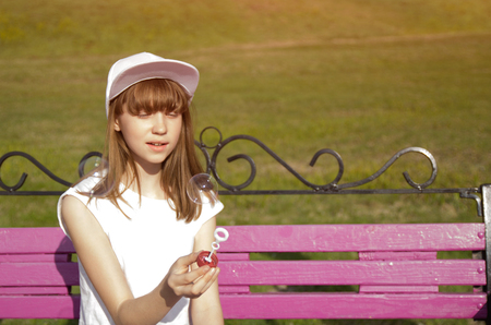 Cute girl is blowing a soap bubbles on the benchの写真素材