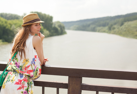 young girl in white dress and straw hat posing at sunset on the river bankの写真素材