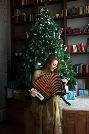 Beautiful girl playing the accordion on a christmas tree background.の写真素材