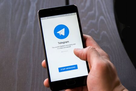 Novosibirsk, Russia - April 30, 2018 - Man holding smartphone with Telegram logo on screen, wooden...