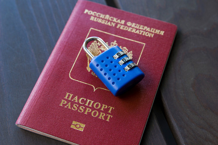 Blue lock lying on the red passport on a wooden background, close-up.の写真素材