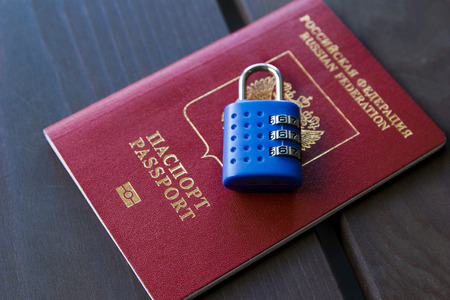 Red Passport with a blue lock on a wood background, close-up.の写真素材