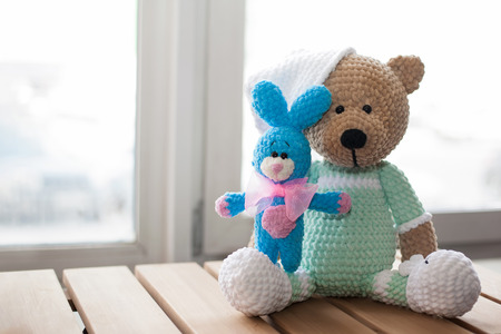 Brown stuffed animal teddy bear and small knitted blue rabbit on the wood. Copy space.
