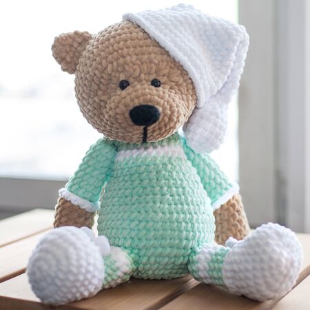 Handmade amigurumi teddy bear on wooden table.の写真素材