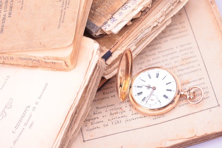 Antique vintage gold pocket watch closeup on a background of old books, the biblical text and the cover of a book printed before 1914の写真素材
