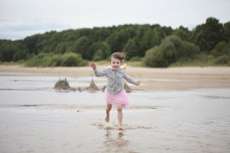 Little girl running in waves on sand against the shoreの写真素材