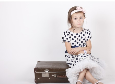 Little girl sitting on an old suitcase on white backgroundの写真素材