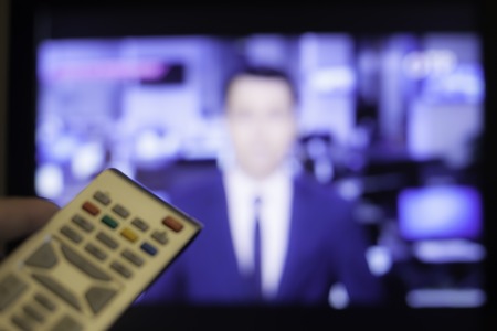 Hand holding TV remote control with a television in the background. Close up.の写真素材