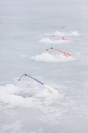 winter fishing rods over the holes on the ice of the pondの写真素材