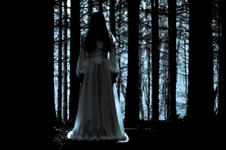 Woman with long black hair in white dress in the spooky dark forestの写真素材