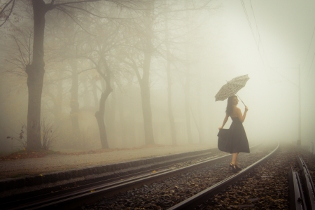 View of a beautiful woman with black dress and umbrella on a train tracks