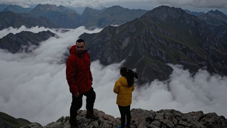 Two adventurers standing on mountain peak above clouds dramatic moody atmosphere achievement hiking...