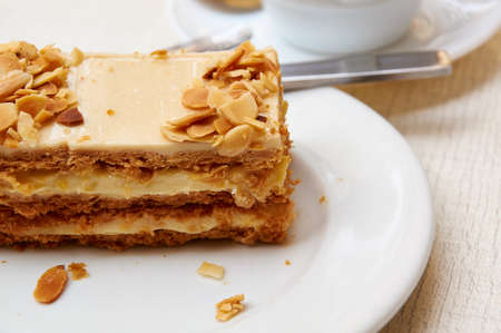 A piece of puff honey cake or a pie with almonds on a white plate. Almond pie in the bar on a white...
