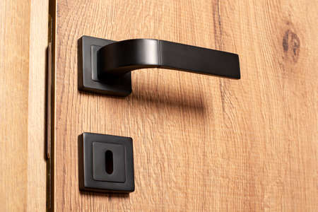 Close-up interior door handle. Wooden door with black door handle