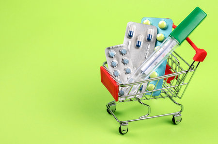Thermometer, pills, tablets and vitamins in a shopping cart on green background. Concept: shopping and delivery of medicinesの写真素材