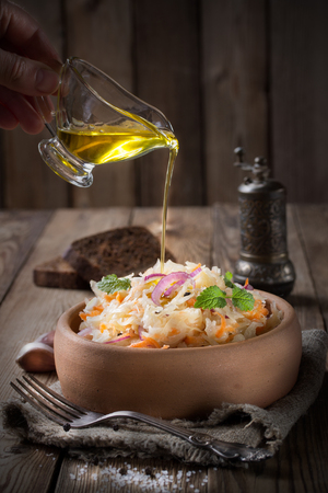 Sauerkraut with onions and mint, in a pottery,pour olive oil. Pieces of black rye bread and a pepper shaker on the back of a wooden background.の写真素材