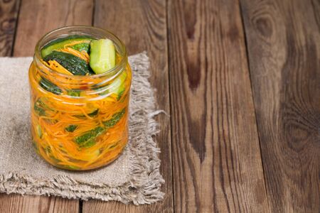 Fermented canned cut cucumbers in a jar on a wooden table. Traditional Korean snack of kimchi cucumbers. Copyspaceの写真素材