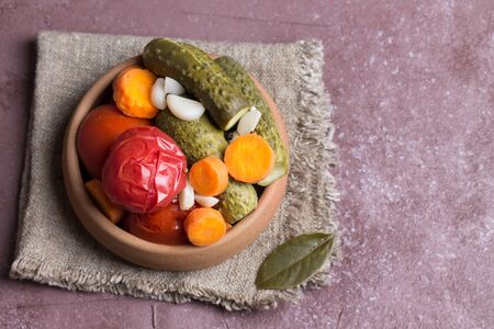 Pickled tomatoes and cucumbers in pottery on a blurred pink background.の写真素材