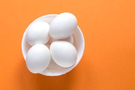 A few white eggs in a bowl on a colorful terracotta background. Image contains copy space.