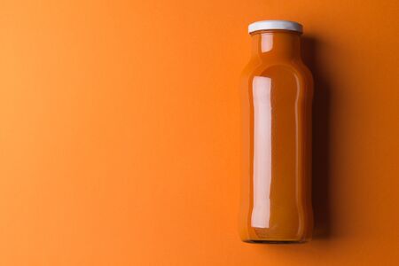 Carrot juice in a glass bottle on an orange gradient paper background. Minimalism. Image contains copy spaceの写真素材