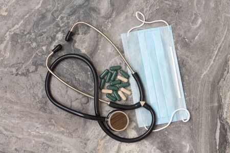 A protective blue mask and vitamins in the form of capsules, a phonendoscope lie on a gray marble...