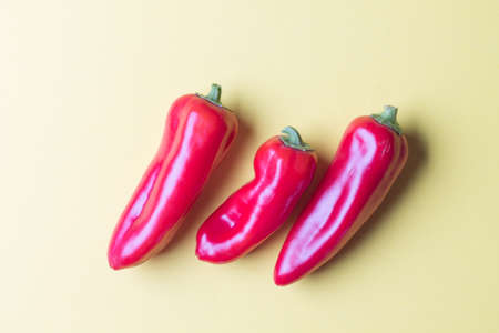 Three ripe red bell peppers on a bright yellow background.の写真素材