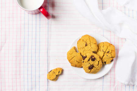 Dessert cookies made of corn flour with raisins with a red cup of milk, on a light background, with copy space.の写真素材