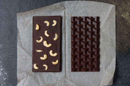 Two bars of natural vegan milk chocolate with cashew nuts on parchment paper.