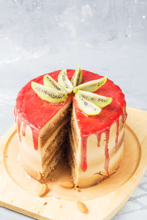 Gluten-free cake with strawberry frosting, coconut chips and almonds on a stand, decorated with kiwi...