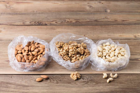 Walnuts, almonds, cashews in plastic bags on a natural wooden background. Copy space. Superfoodsの写真素材