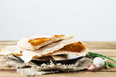 The broken pita bread on flour sourdough lies on a napkin, on a wooden table, along with green...