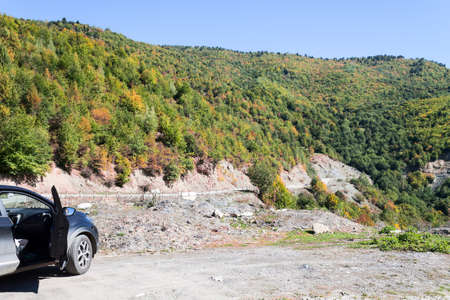 A black car stands at a halt on the road to Mestia. Wooded mountains.