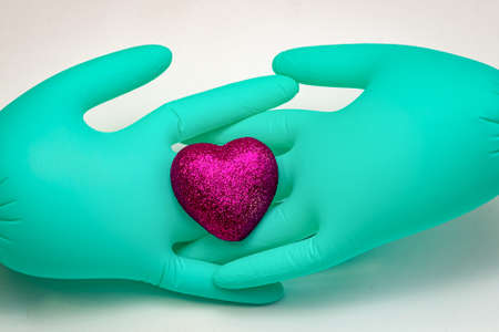 A pair of green medical gloves are intertwined fingers and hold a scarlet heartの写真素材