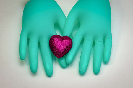 Surgical gloves of green color are connected by fingers and scarlet heart is on themの写真素材