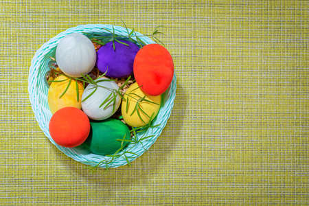 Easter painted colored eggs with green sprigs in a wicker basket on green burlap, top view