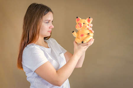 A girl 14-15 years old is holding a piggy bank and looking at it. Selective Focusの写真素材