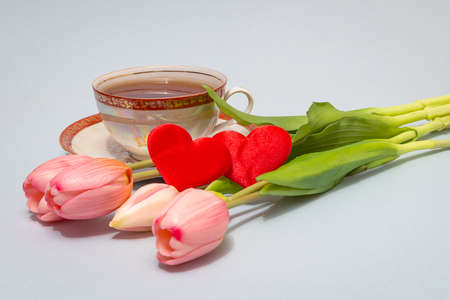 Tea in an antique porcelain cup, a bouquet of pink tulips, a pair of scarlet heartsの写真素材