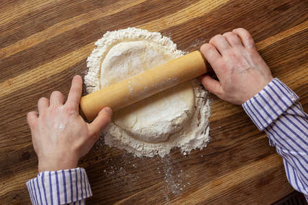 A man rolls out dough on a wooden table, top view. High quality photo