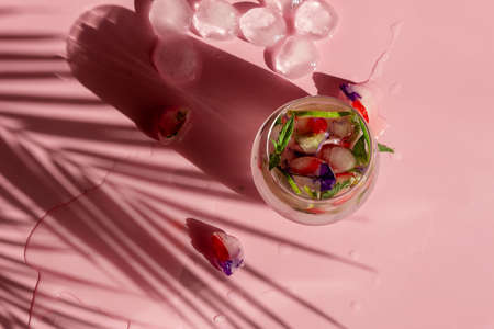 Non-alcoholic cocktail with frozen strawberries, mint and flowers on a pink background, beautiful shadows. Place for your text.の写真素材
