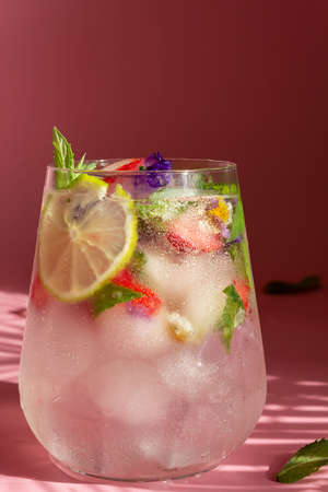 Non-alcoholic cocktail with frozen strawberries, mint and flowers on a pink background. Place for your text. Vertical photo.の写真素材