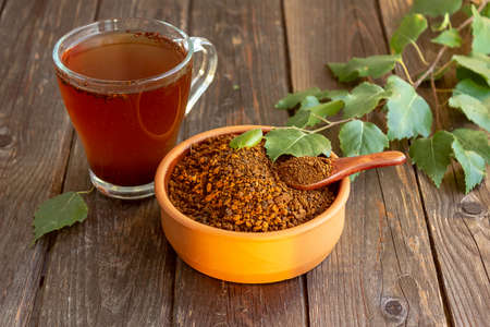 A cup of chaga tea on a dark table, slices of chaga and a birch twig. Selective focus