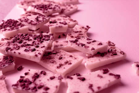 Trendy pink or ruby chocolate with pieces of berries and fruits on a pink background