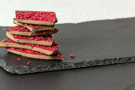 Pieces of milk chocolate with pieces of berries and fruits lie on top of each. Selective focus,...